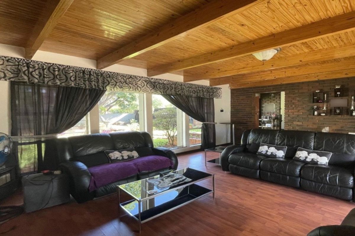 Spacious living room featuring a warm exposed timber beam ceiling, an exposed brick feature wall, and large windows providing natural light and garden views.