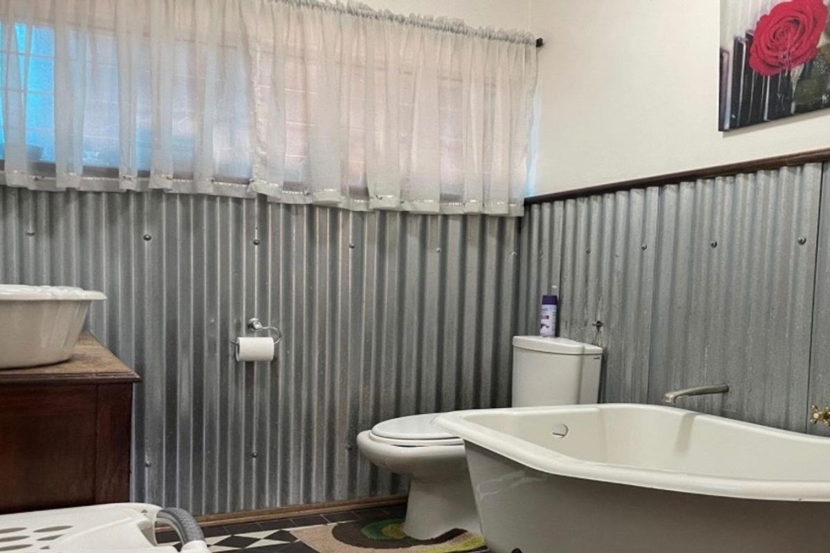 Bathroom featuring a freestanding bathtub, toilet, and unique corrugated metal wall cladding with checkered floor tiles.