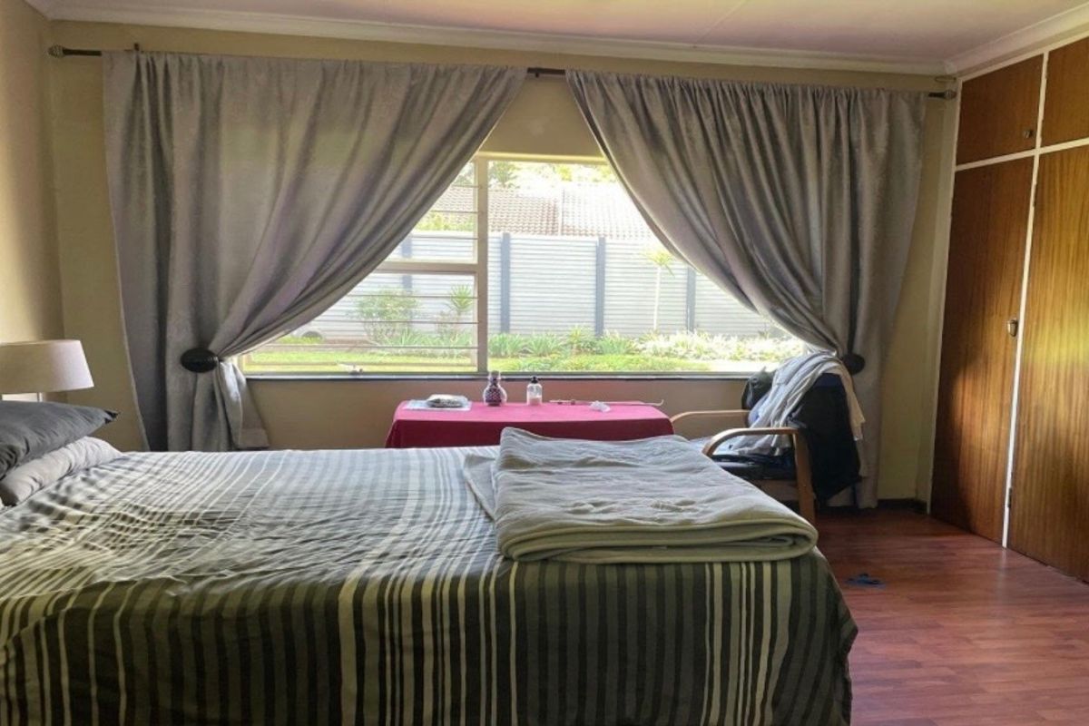 A spacious bedroom featuring laminate flooring and built-in wooden cupboards, offering a functional layout with natural light from a large window.