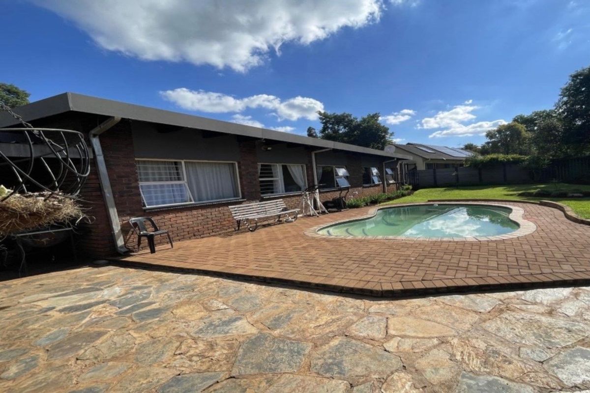 Rear exterior view featuring a swimming pool, brick and stone paved patio areas, and a well-maintained lawn against the brick house facade.