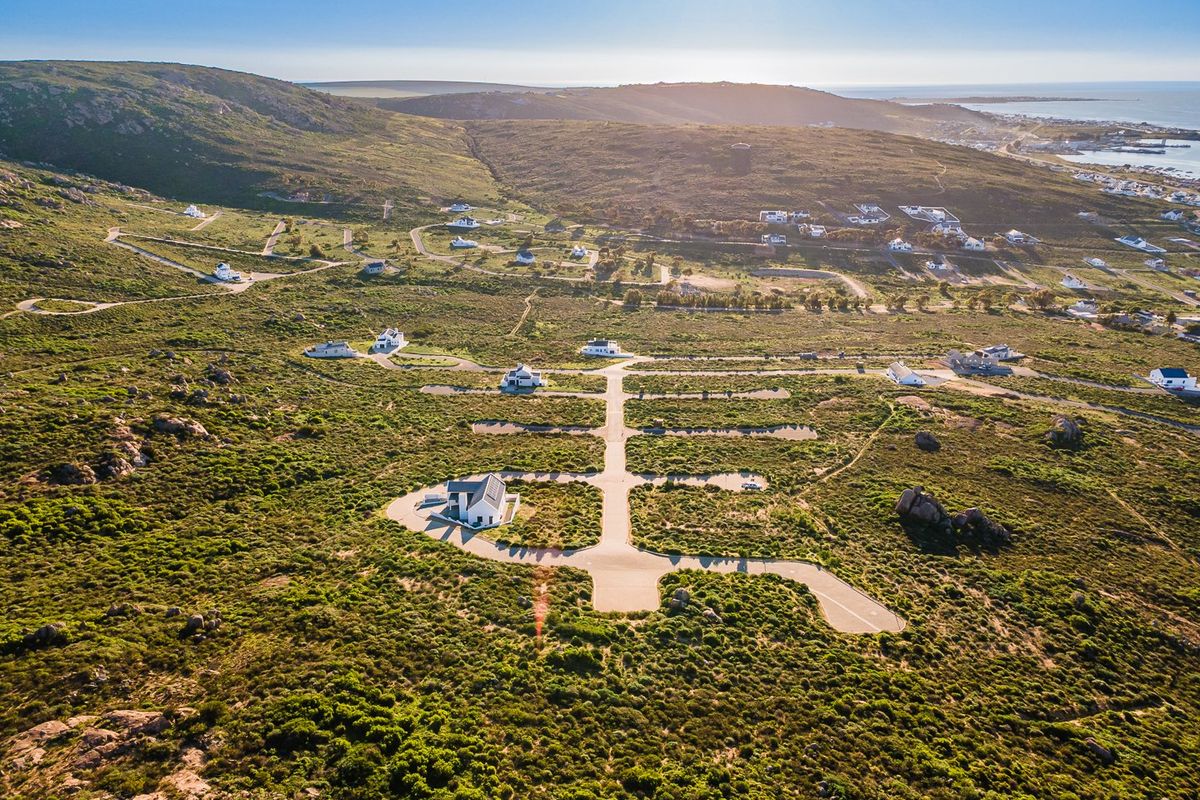 Aerial view of a coastal residential development featuring paved roads and established plots set within a natural landscape.