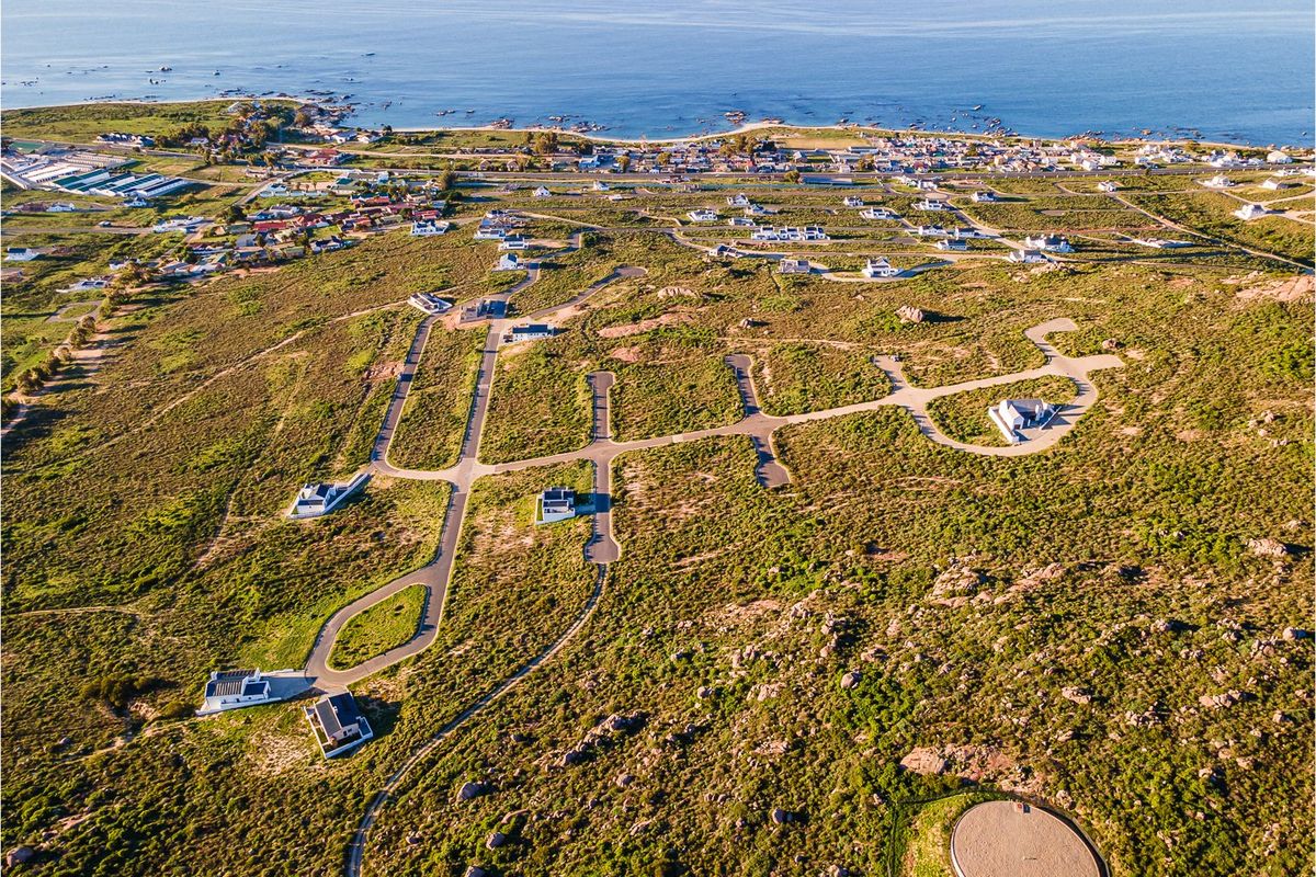 An aerial view of a coastal residential development featuring paved roads and scattered homes set within a natural landscape near the ocean.