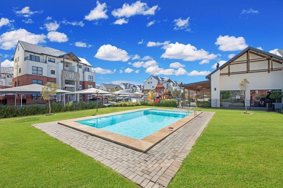 A well-maintained communal swimming pool area featuring a paved surround, manicured lawn, and surrounding apartment complex infrastructure.
