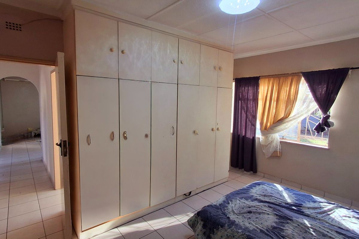 A bedroom featuring extensive built-in cupboards, tiled flooring, and natural light, offering a functional space with potential for cosmetic updates.