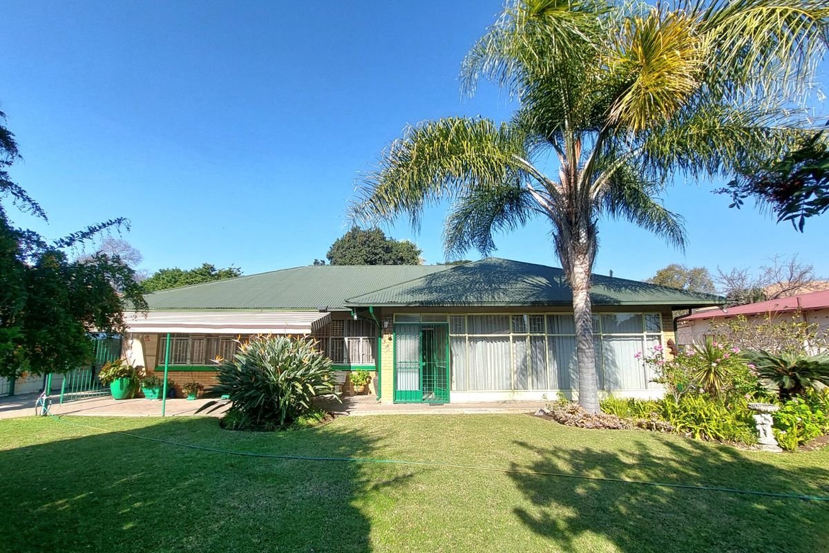 Rear view of the house featuring a metal roof, brick exterior, paved patio area, and established garden with a large palm tree.