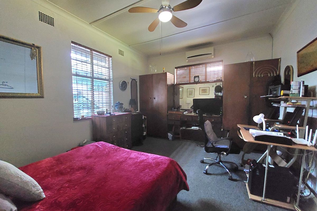 A functional bedroom featuring a ceiling fan, split-system air conditioning, and built-in wardrobe storage with natural light through venetian blinds.