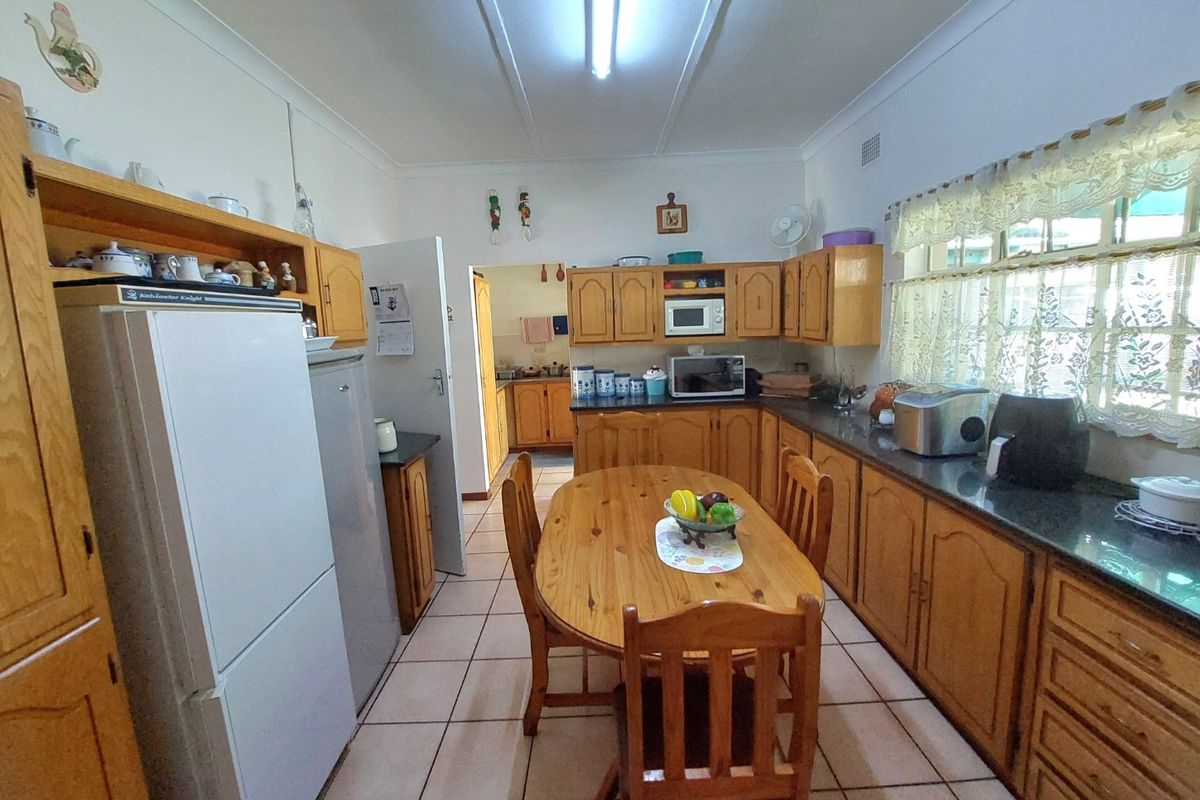 A functional kitchen featuring wooden cabinetry, granite countertops, and tiled flooring, with an adjacent scullery area visible through the doorway.