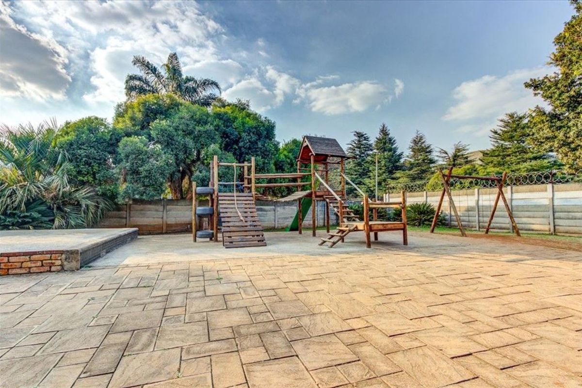 Spacious outdoor garden area featuring paved patio flooring, a precast concrete boundary wall with security fencing, and established trees.