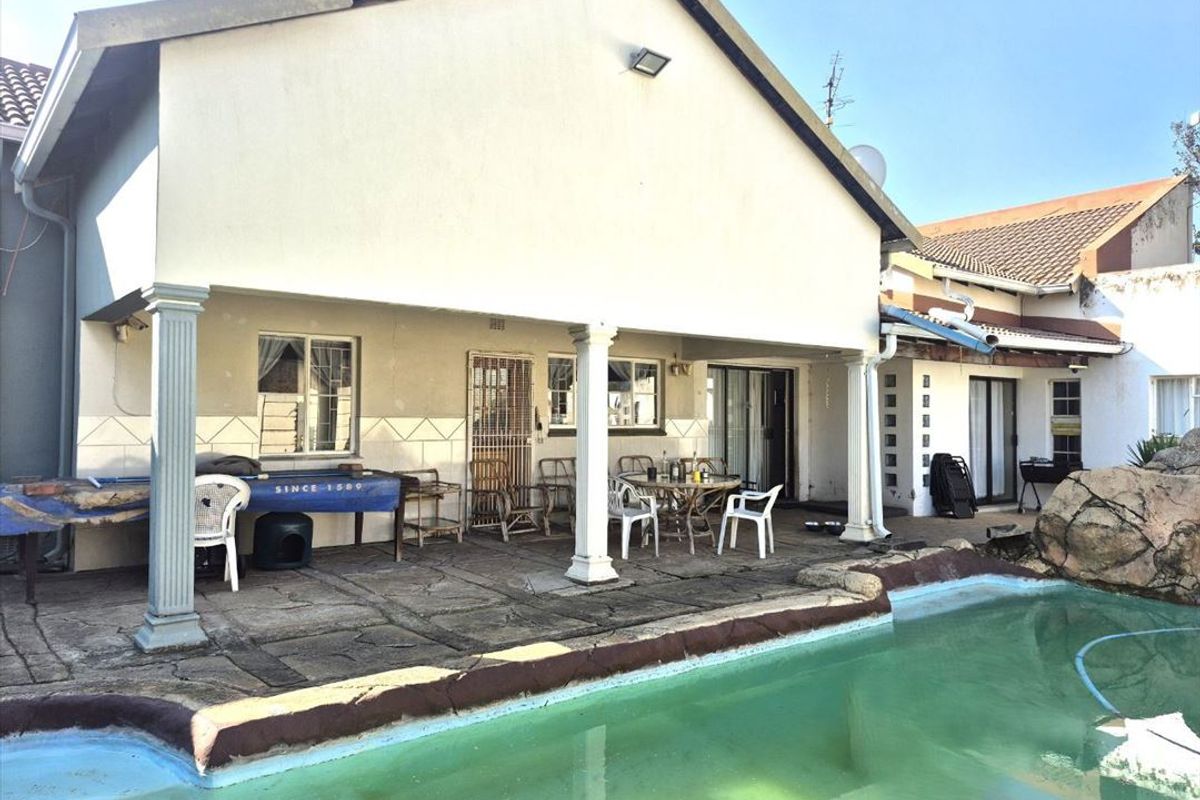 Rear exterior view featuring a covered patio area overlooking a swimming pool with established structural elements and paved surrounds.