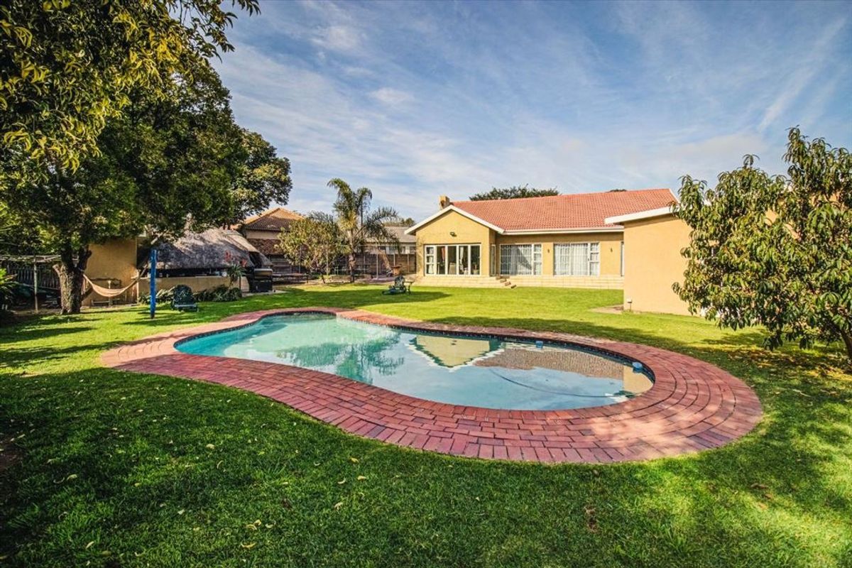 Spacious rear garden featuring a swimming pool with brick coping, a well-maintained lawn, and a detached thatched lapa area.