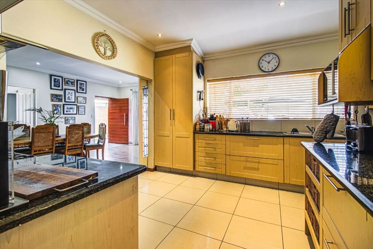 A functional kitchen featuring light wood cabinetry, dark granite countertops, tiled flooring, and an open-plan layout connecting to the adjacent dining area.