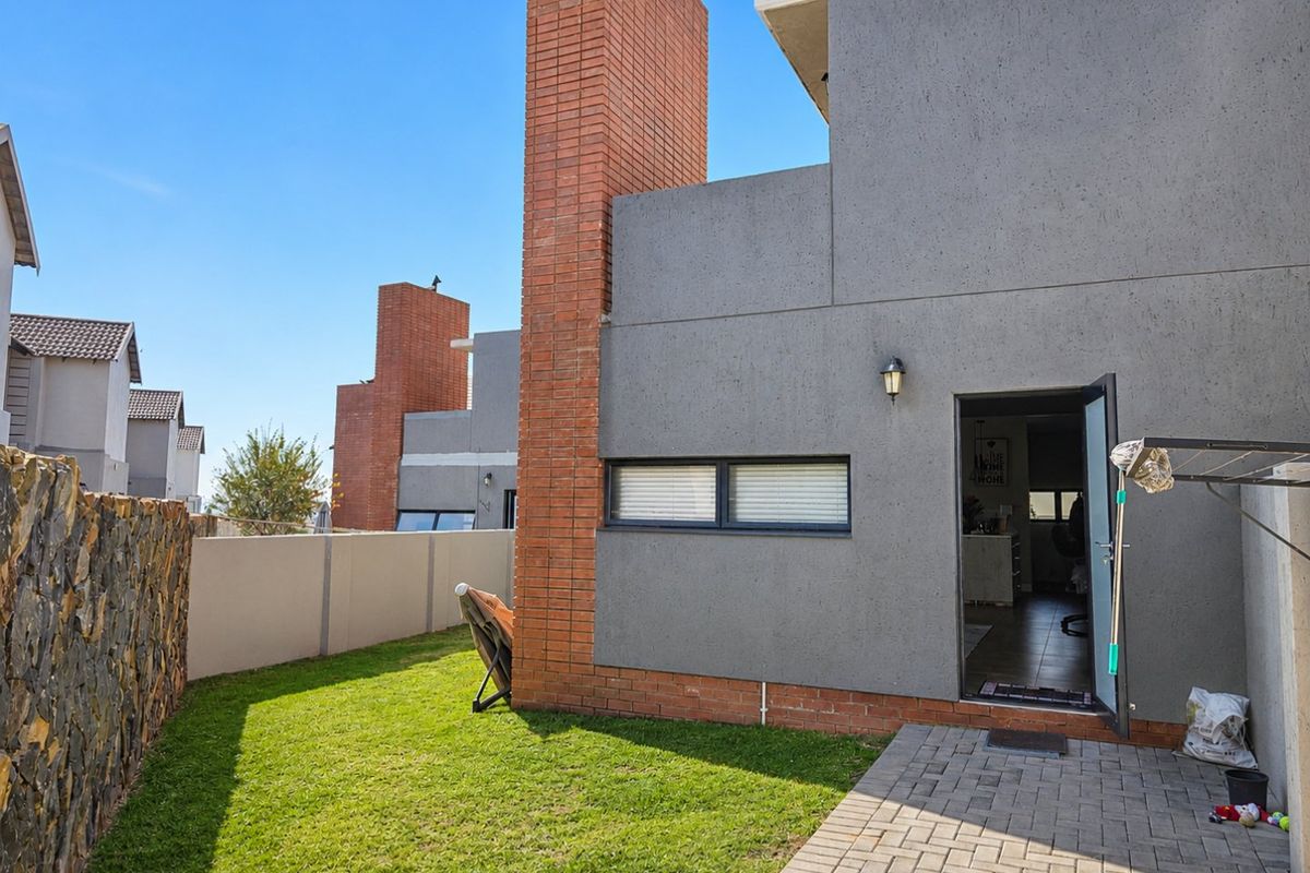 Rear view of the townhouse featuring a private garden, paved patio area, and a prominent brick chimney stack.