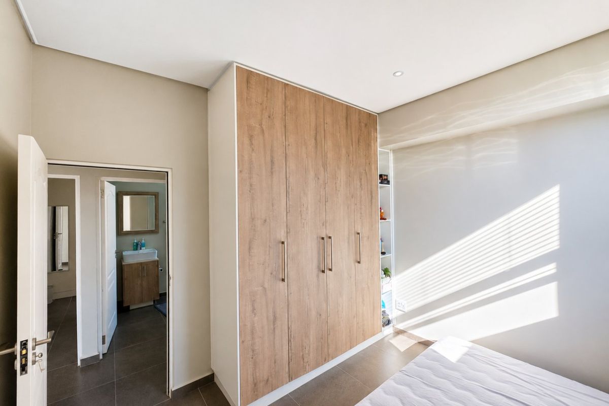 Modern bedroom featuring a large wood-finish built-in wardrobe with integrated shelving and direct access to an en-suite bathroom with tiled flooring.
