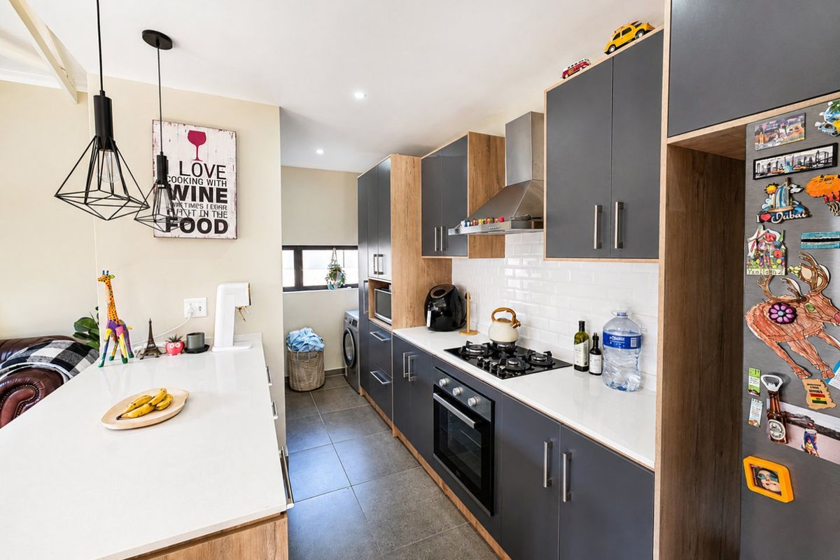 Modern kitchen featuring dark grey cabinetry, wood-tone accents, quartz countertops, gas hob, built-in oven, and a subway tile backsplash.