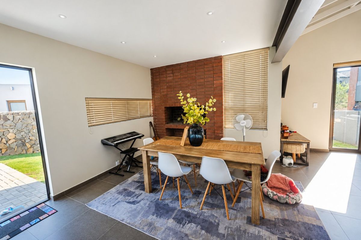 Spacious living area featuring a prominent exposed brick fireplace, vaulted ceilings, tiled flooring, and large sliding glass doors providing access to the garden.
