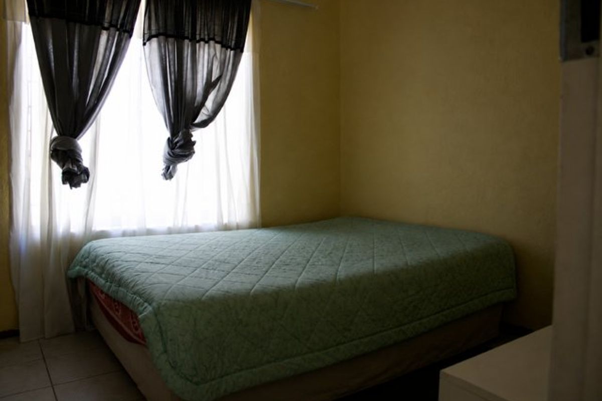 A compact bedroom featuring tiled flooring and a window with curtains, providing a functional sleeping space.