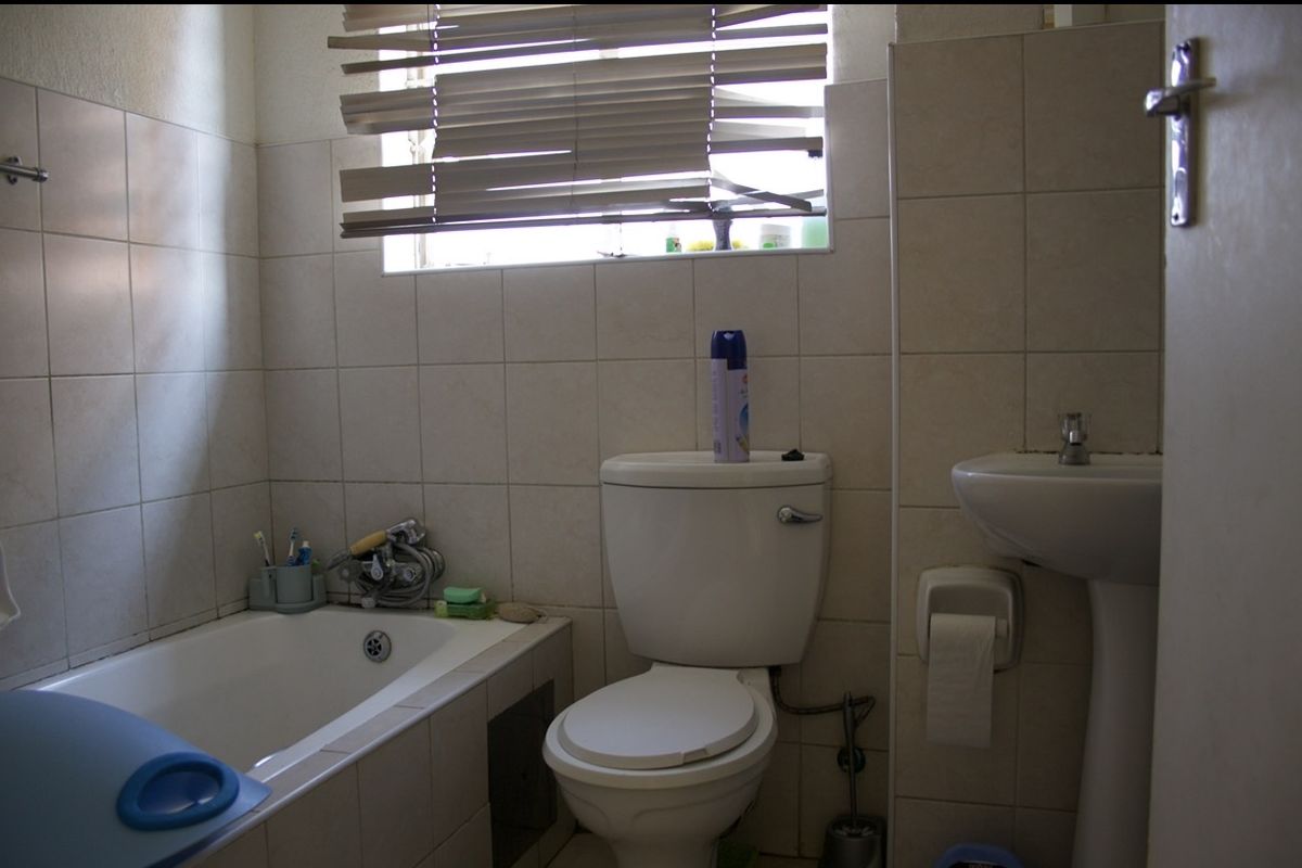 A functional bathroom featuring a bathtub, pedestal basin, and toilet with neutral wall tiling.