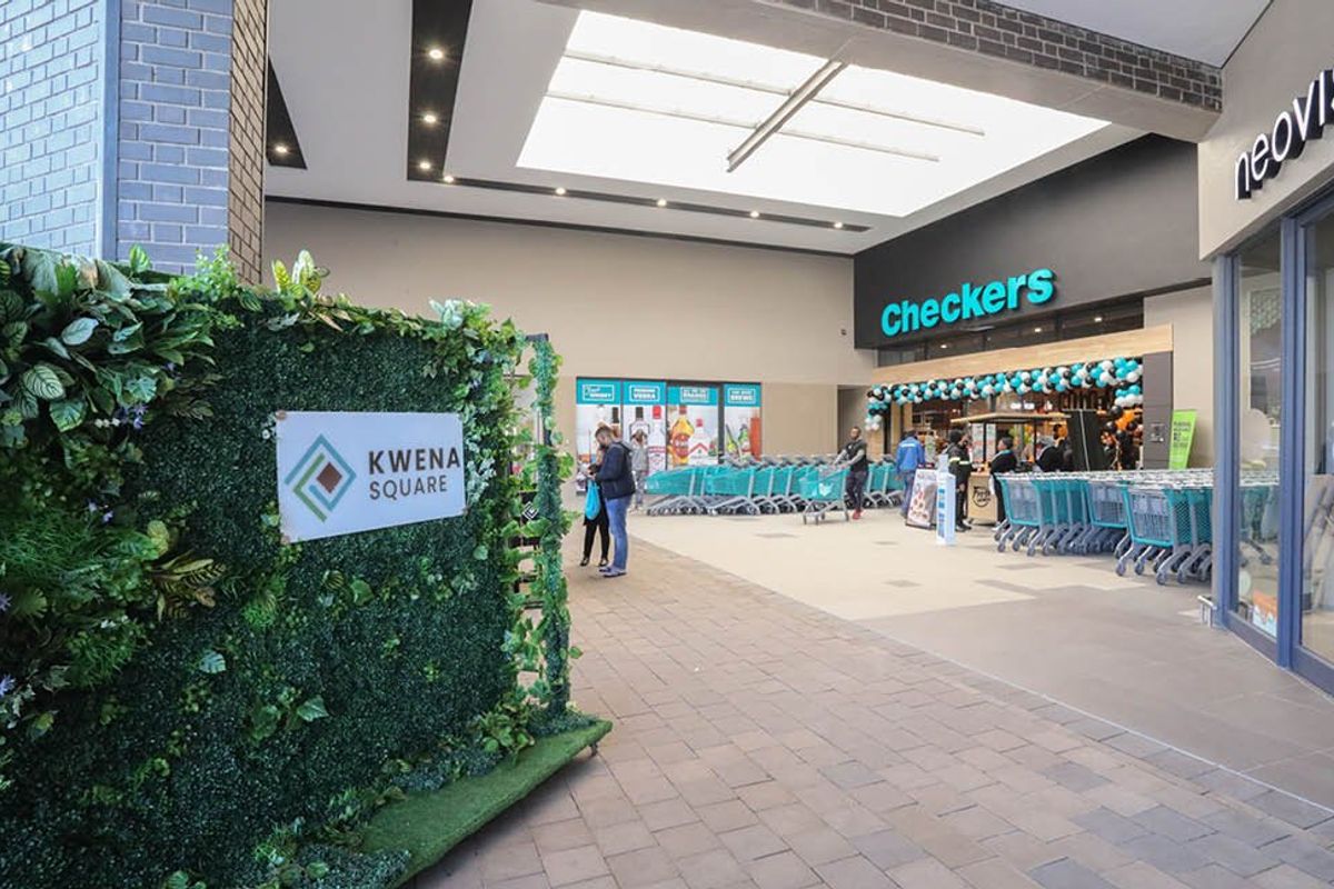Modern commercial shopping center entrance featuring tiled flooring, a large skylight, and glass storefronts for retail units.