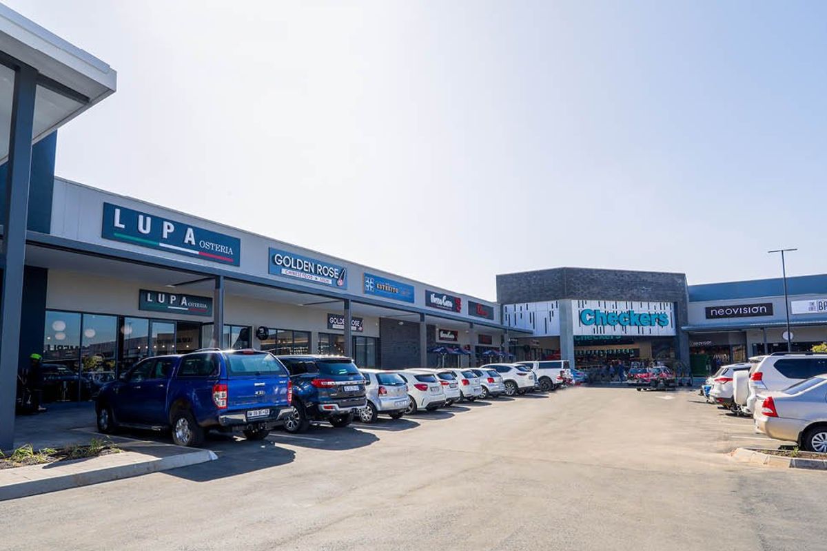 A modern commercial shopping center exterior featuring multiple retail storefronts, prominent signage, and a paved parking lot for customer access.