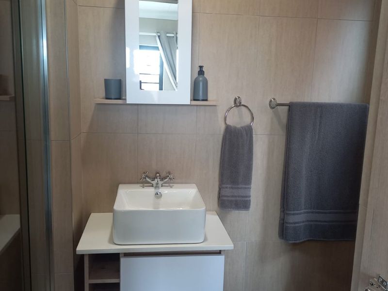 A modern bathroom featuring a vessel sink with vanity cabinet, wall-mounted medicine cabinet, shower enclosure, and neutral ceramic wall tiling.