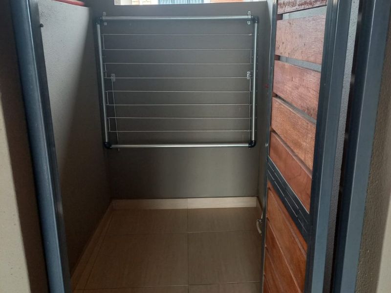 A functional outdoor laundry or utility area featuring tiled flooring, a wall-mounted drying rack, and a secure timber and metal access gate.