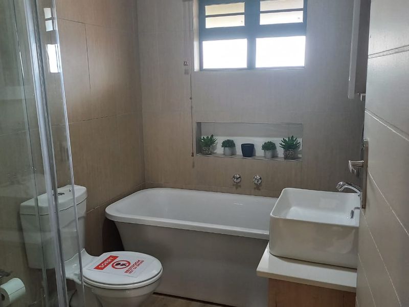 A modern bathroom featuring a freestanding bathtub, glass-enclosed shower, vanity with basin, and neutral wall tiling with a convenient recessed storage niche.