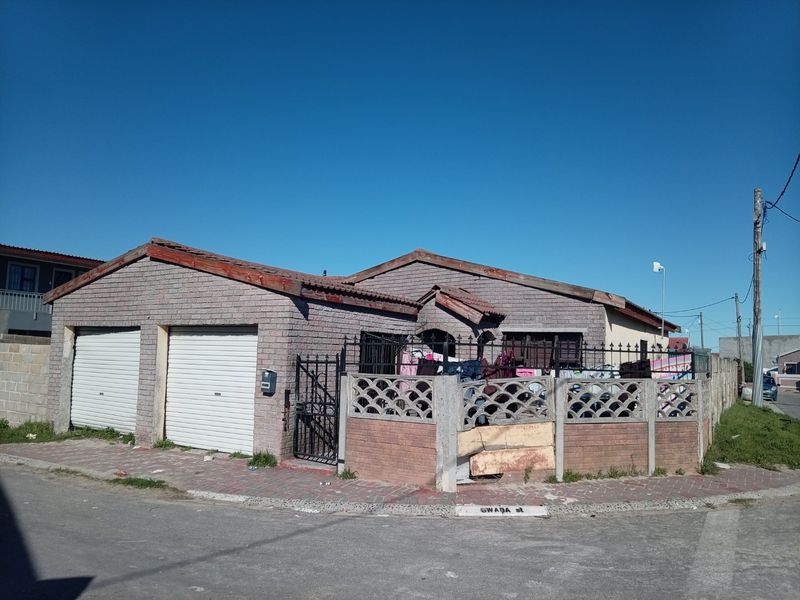 Front exterior view of a single-story house featuring a double garage with roller shutter doors and a perimeter wall with a gated entrance.
