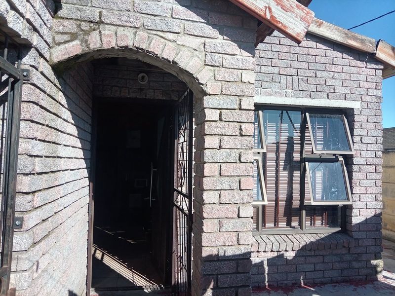 Front entrance of a brick house featuring an arched doorway, security gate, and top-hung window with visible weathering on the timber fascia.