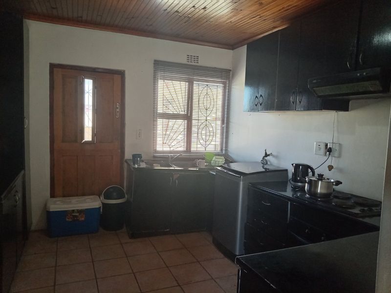 Functional kitchen featuring dark cabinetry, tiled flooring, timber ceiling, and integrated hob with extractor fan.