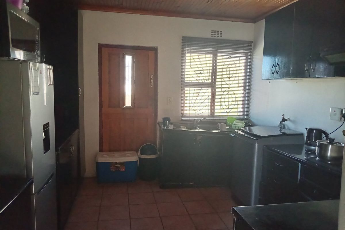 A functional kitchen featuring dark built-in cabinetry, a double sink, tiled flooring, and a timber-paneled ceiling with direct access to the exterior.