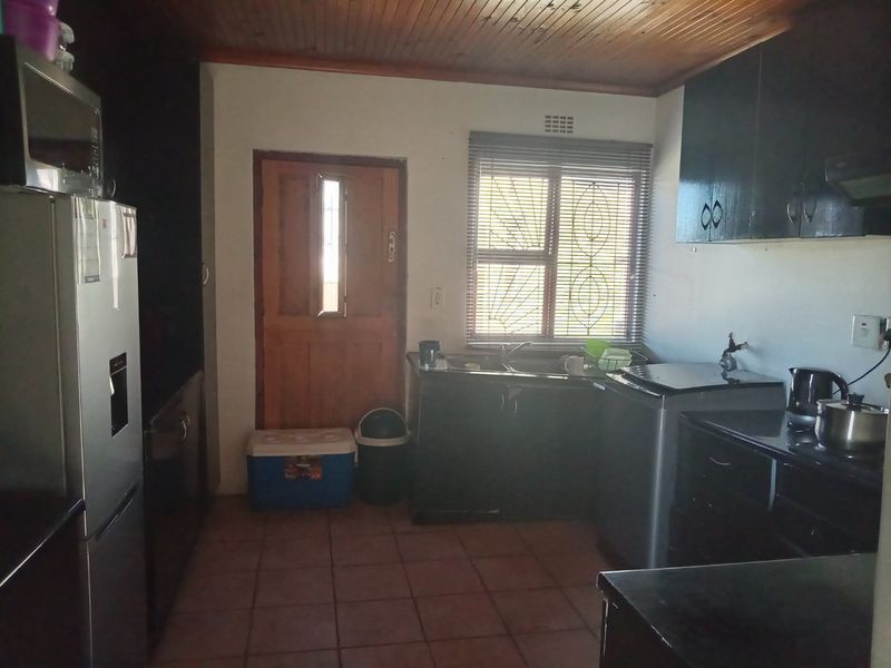 A functional kitchen featuring dark built-in cabinetry, a double sink, tiled flooring, and a timber-paneled ceiling with direct access to the exterior.