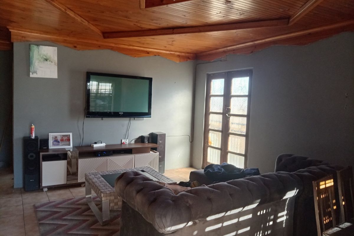 A living room featuring a distinctive timber-clad vaulted ceiling, tiled flooring, and access to the exterior via classic french doors.