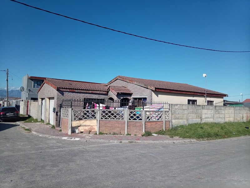 Front exterior view of a single-story brick house featuring a tiled roof, garage, and perimeter boundary walling on a corner plot.