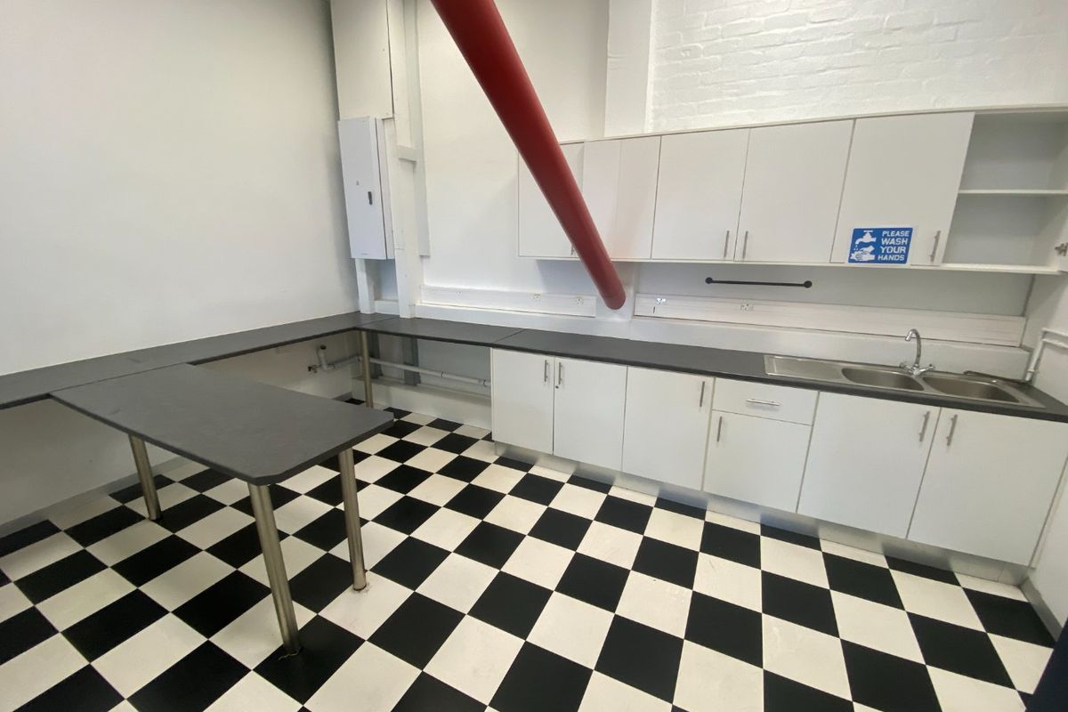 A functional commercial kitchen space featuring white cabinetry, dark countertops, a stainless steel sink, and distinctive checkerboard flooring.