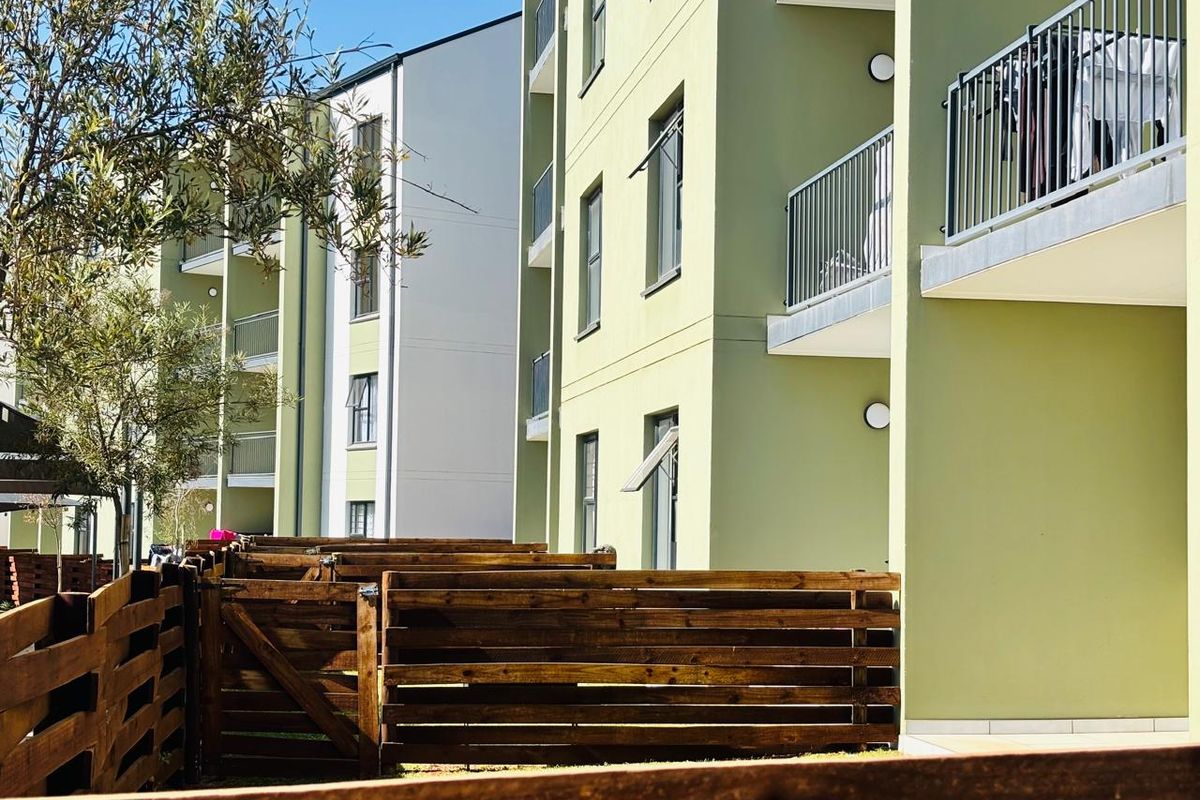 View of the apartment complex rear facade featuring private balconies with metal railings and ground-level timber fencing.