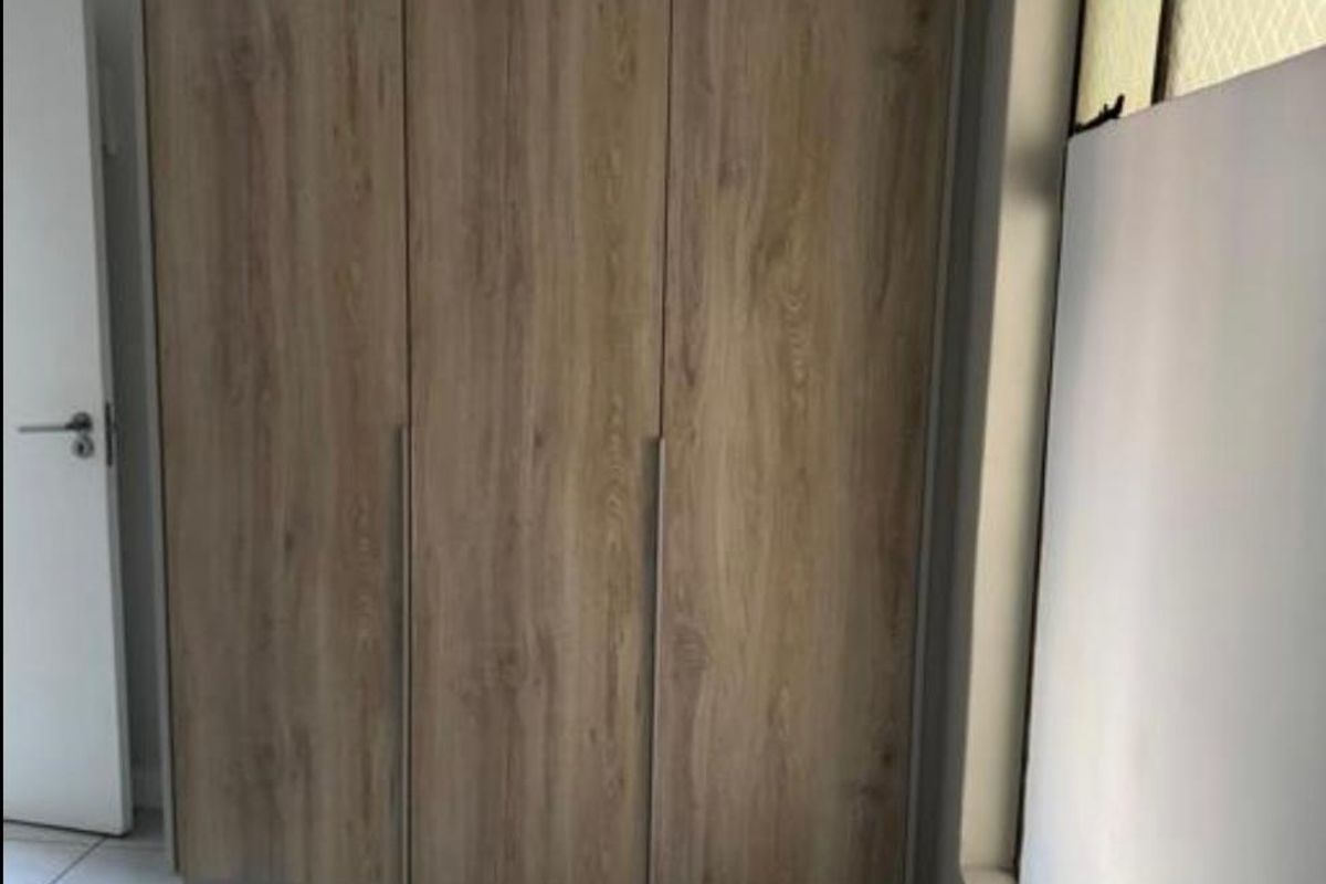 A bedroom featuring modern wood-finish built-in wardrobes and neutral tiled flooring, offering clean and functional storage space.