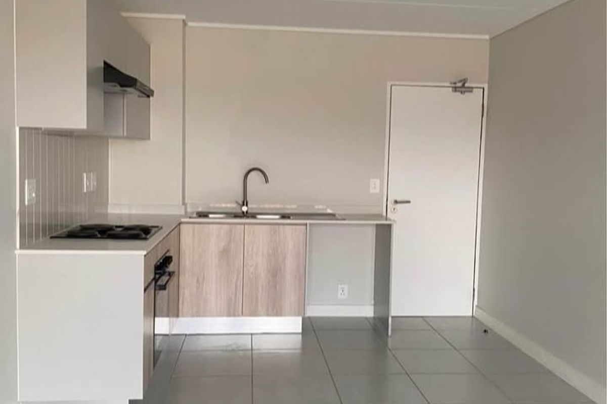 A clean, modern kitchen featuring light wood-tone cabinetry, a built-in hob and oven, tiled backsplash, and neutral floor tiles in an open-plan layout.