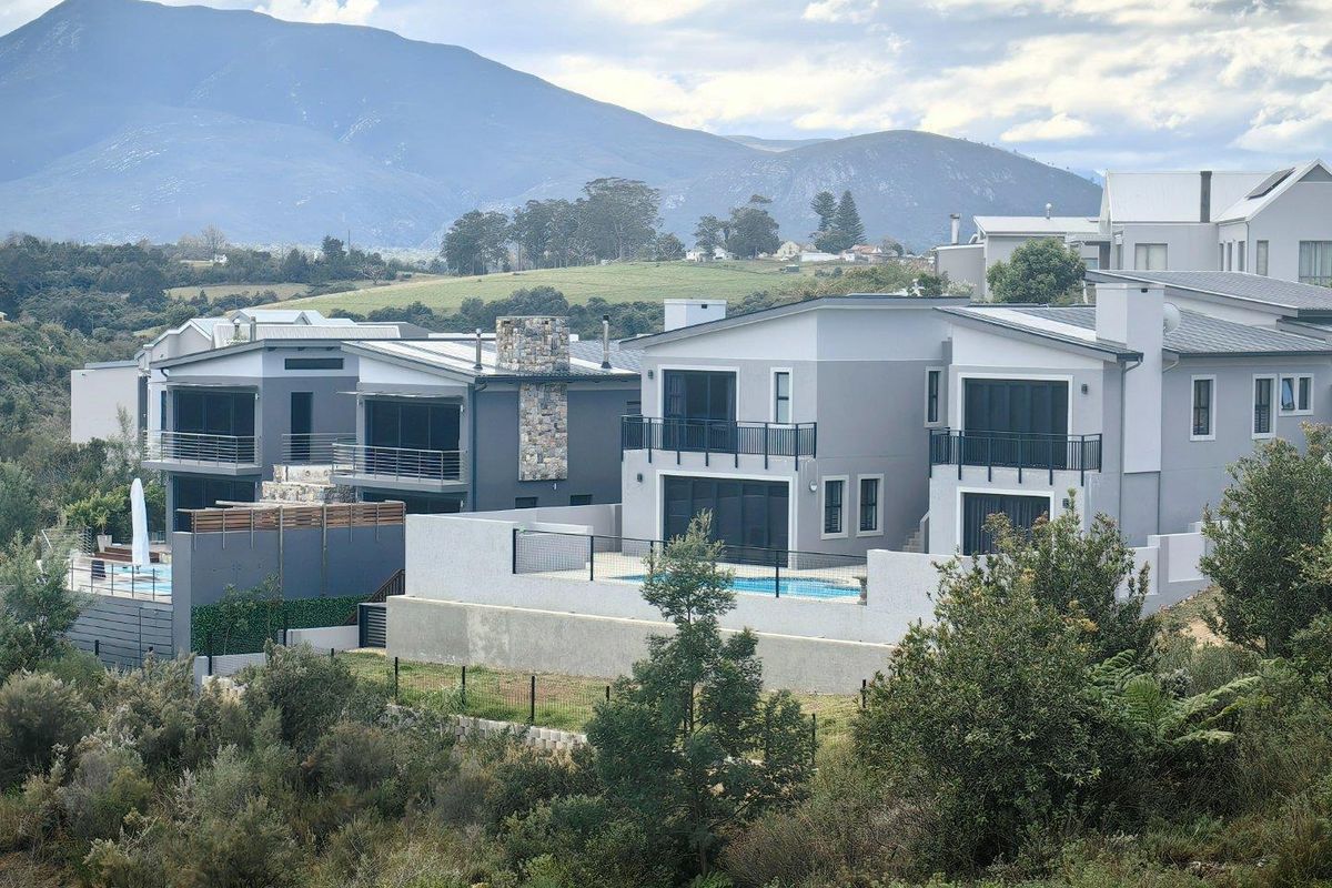 Rear view of modern multi-story residential homes featuring balconies, swimming pools, and stone chimney details set against a scenic mountain backdrop.