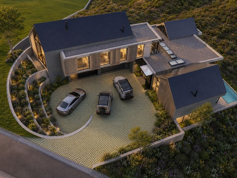 Aerial view of a modern architectural house featuring a metal roof, integrated skylights, a paved driveway, and a private swimming pool.