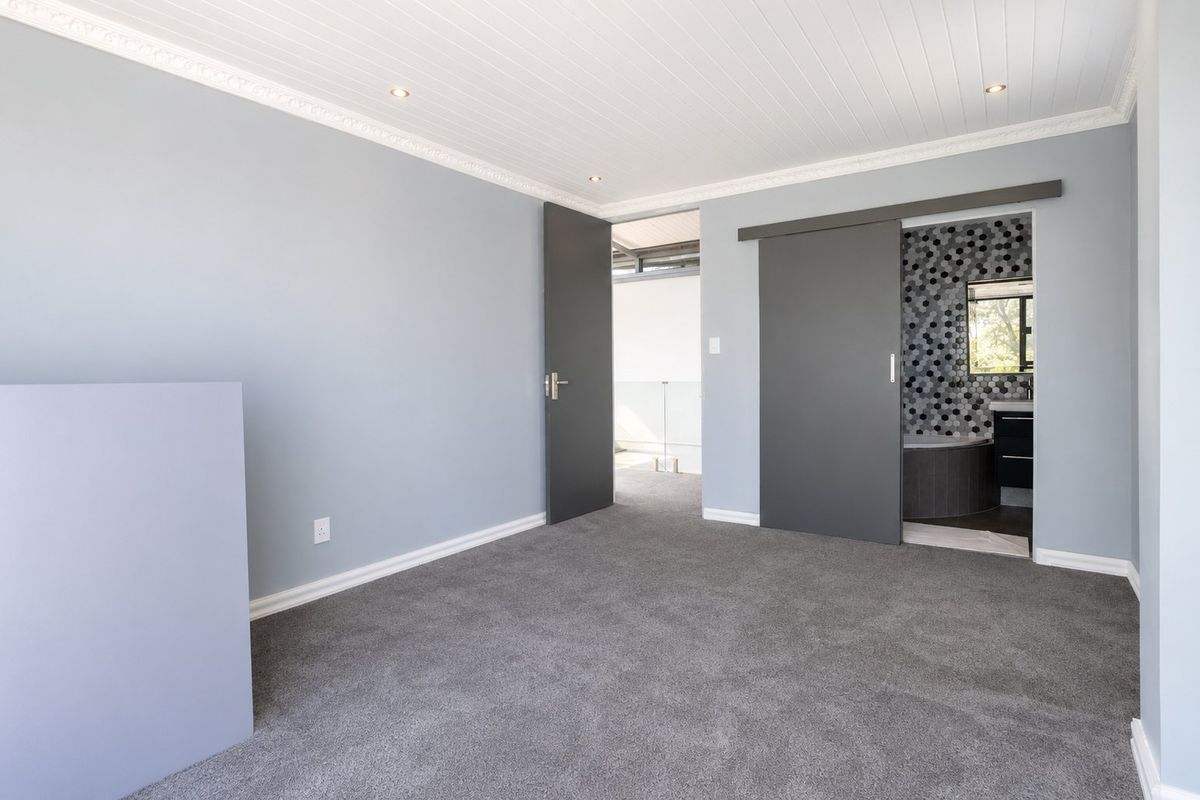A clean, empty bedroom featuring grey carpeting, crown molding, recessed lighting, and a sliding barn door leading to an en-suite bathroom.