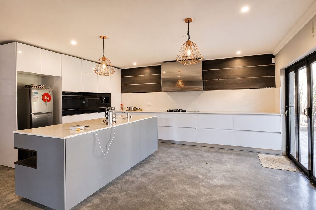 Modern kitchen featuring a large central island, sleek white cabinetry, integrated appliances, stone countertops, and direct access to the outdoor area via sliding doors.