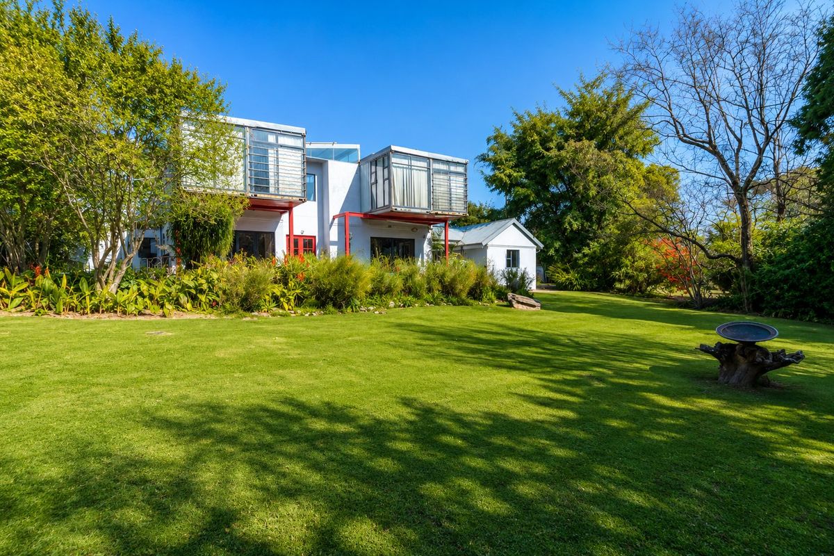 A spacious rear garden featuring a well-maintained lawn and a unique modern architectural home with distinctive cantilevered upper levels.