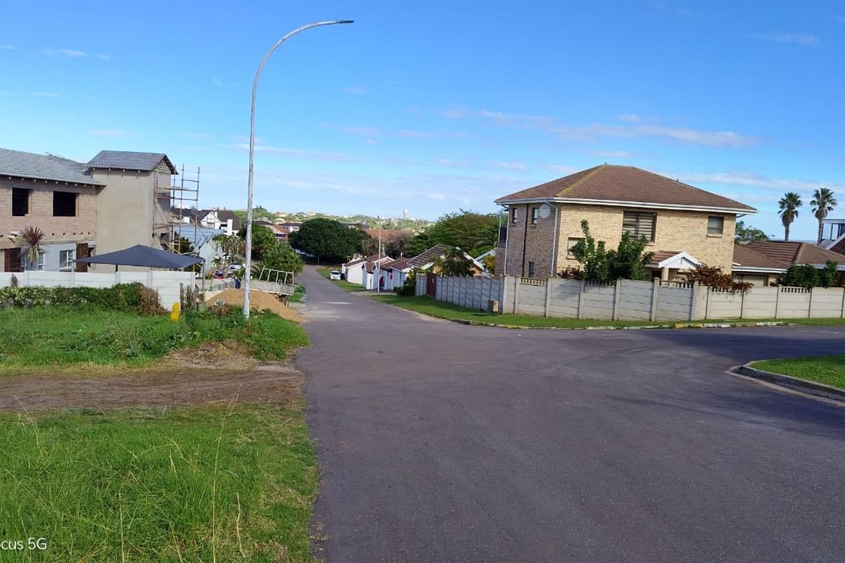 A street view of a residential neighborhood featuring paved roads, street lighting, and established boundary walls surrounding nearby properties.