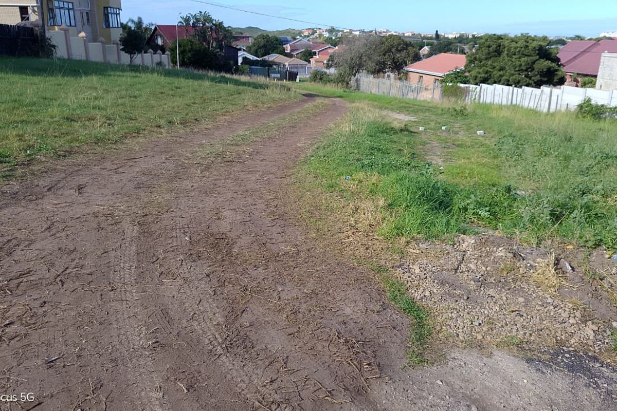 A view of a vacant residential plot featuring an unpaved access road and surrounding grass verge in a developed neighborhood.