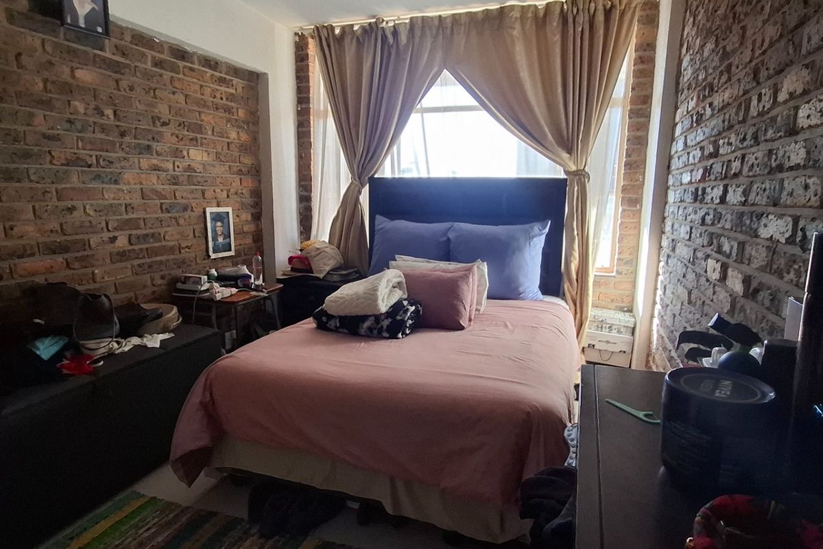 A bedroom featuring exposed brick walls and a large window, providing a unique industrial aesthetic.