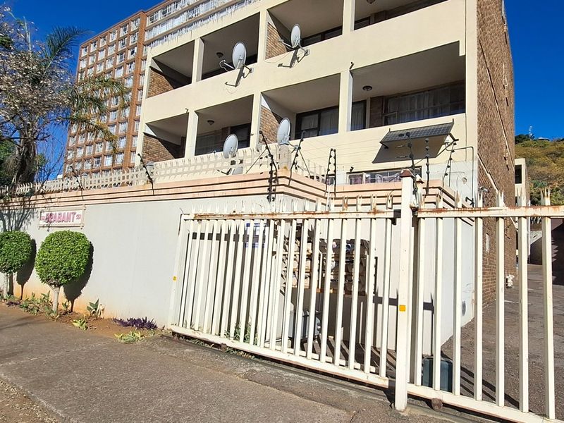 Exterior view of an apartment building featuring a brick facade, balconies, and a secure gated entrance with electric fencing.