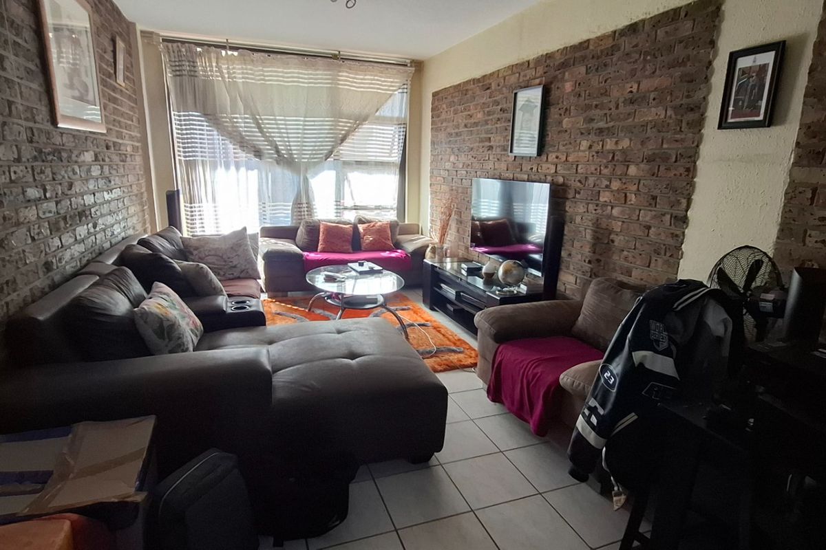 A living room featuring exposed brick feature walls and tiled flooring, with a large window providing natural light.