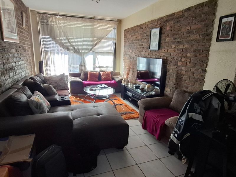 A living room featuring exposed brick feature walls and tiled flooring, with a large window providing natural light.