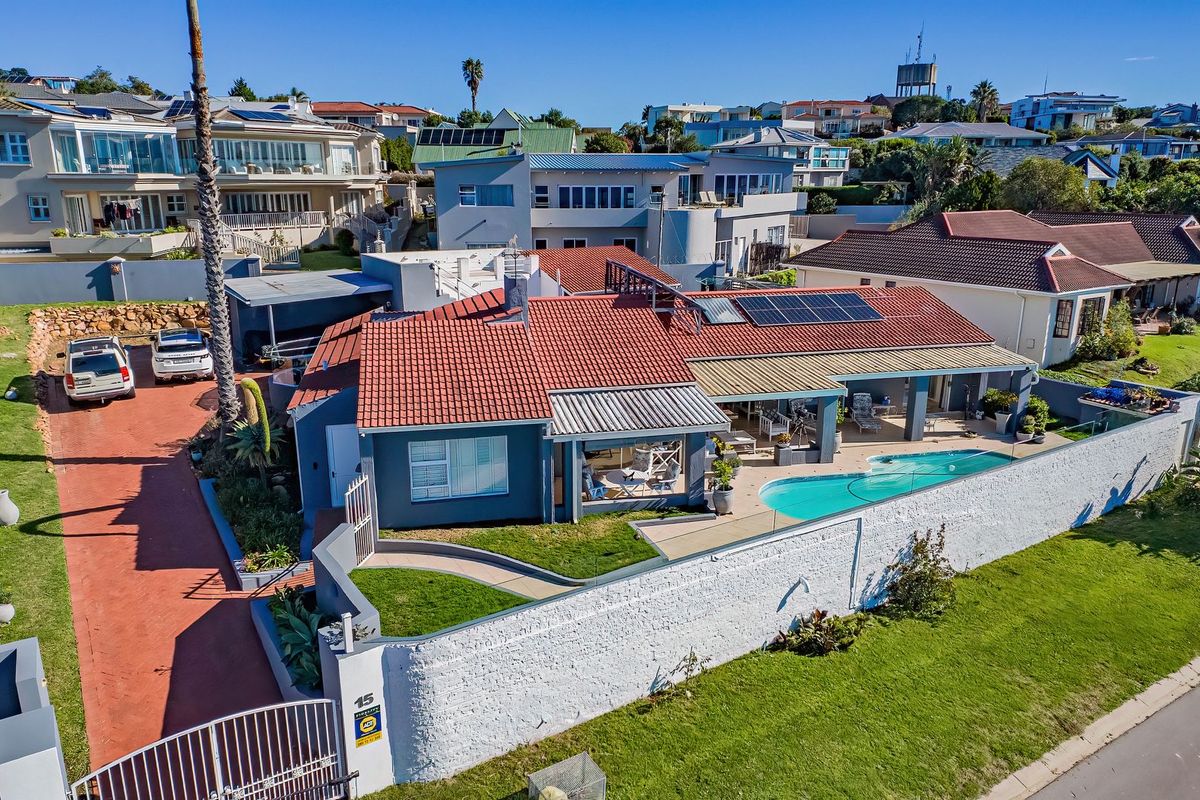 Aerial view of a residential property featuring a swimming pool, covered patio, solar panels, and a secure boundary wall.