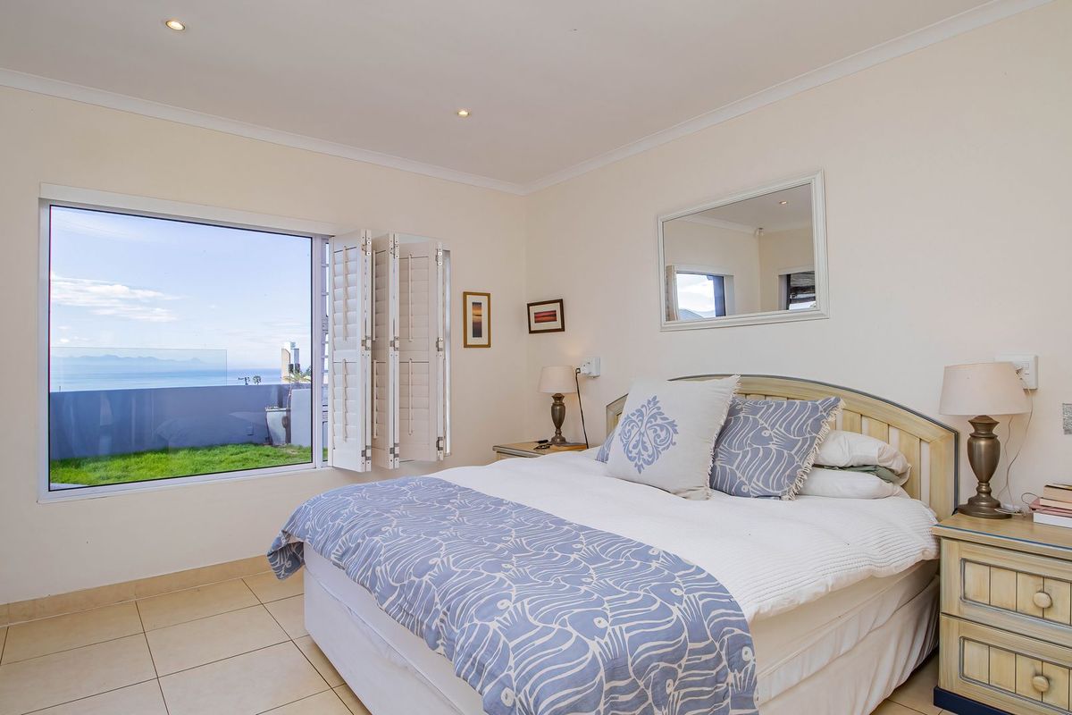 A bright bedroom featuring tiled flooring, recessed lighting, and plantation shutters, offering a clear view of the outdoors.